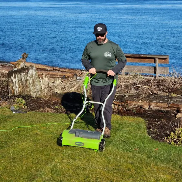 Dave in a Peak to Peak shirt working a waterfront lawn with an electric lawn tool